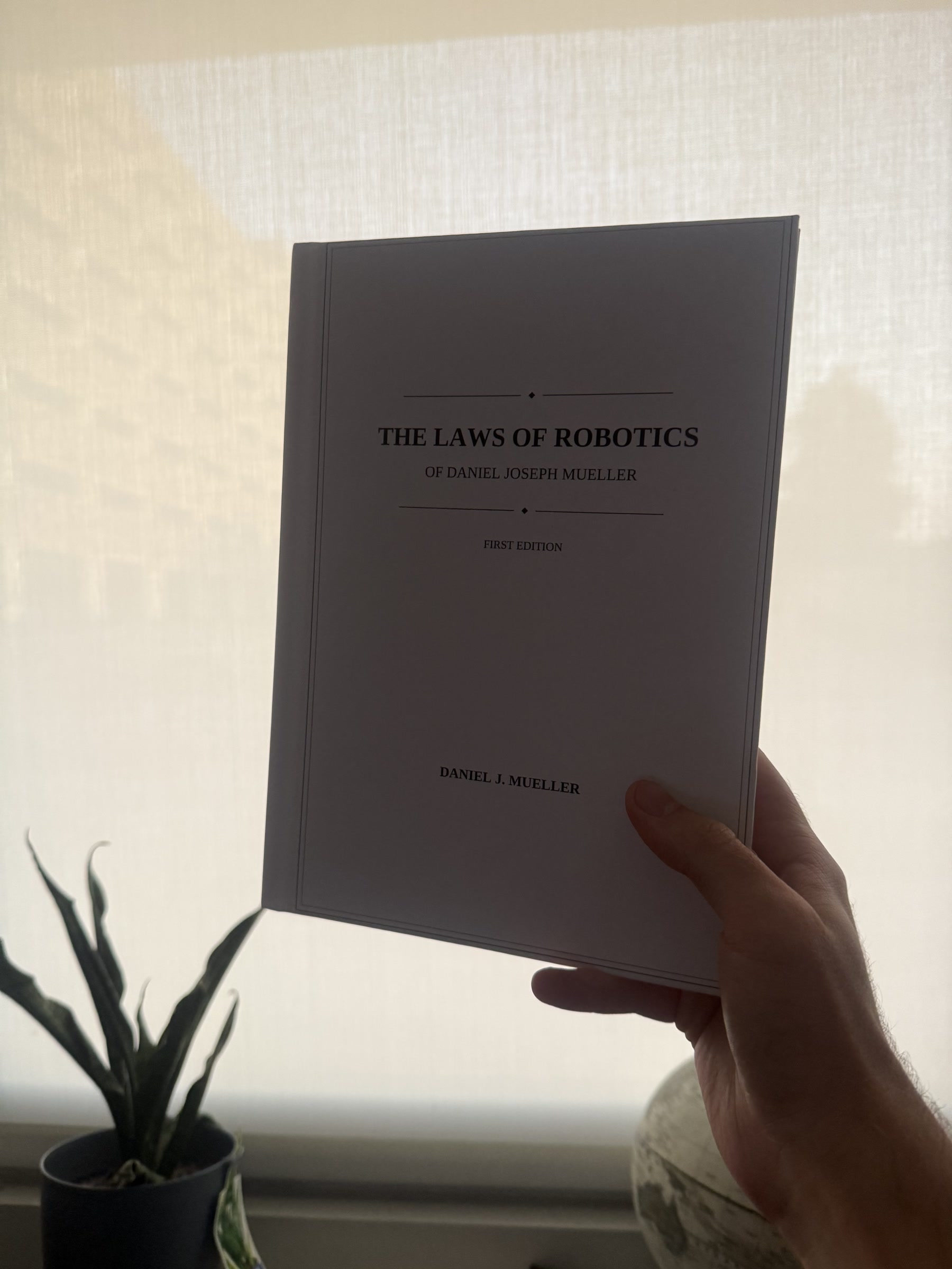 A hand holding Daniel Joseph Mueller’s first-edition book The Laws of Robotics